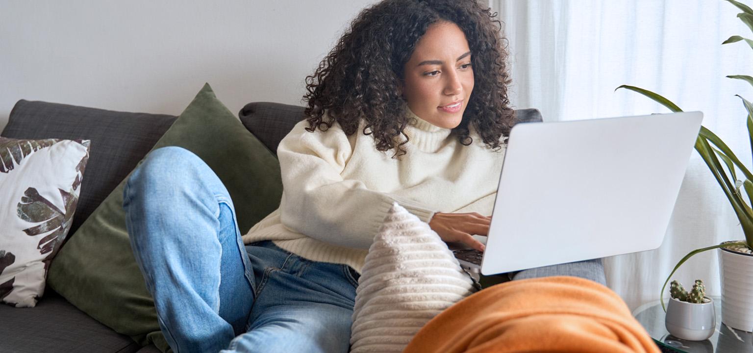 Une jeune femme aux cheveux bouclés s’informe sur les investissements sur son ordinateur portable